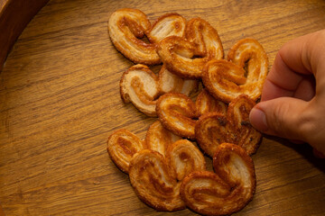 a hand taking delicious freshly baked puff pastry ears on a wood colored board