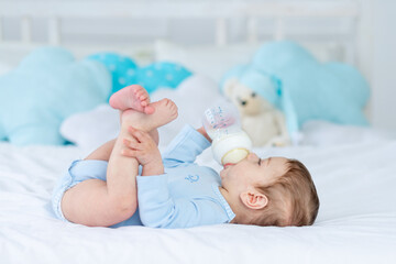 baby boy with a bottle of milk on the bed for sleeping in a blue bodysuit, baby food concept