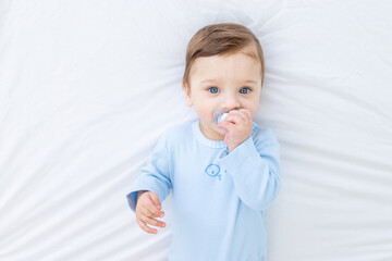baby boy with pacifier on bed before going to bed in blue bodysuit, happy healthy little baby
