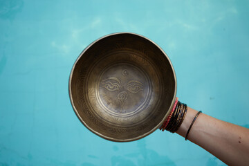 Woman with singing  tibetian bowl in hands with sea background