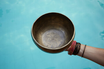 Woman with singing  tibetian bowl in hands with sea background