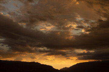 	
Cloudscape. Magical view of a dramatic sunset in the mountains. The beautiful sky, clouds and mountain dark silhouette with dusk colors.