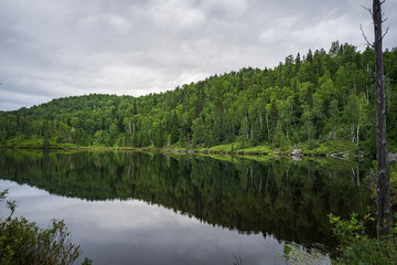 Fototapeta na wymiar Reflections on a cloudy day in the waters of the small Lac des Pères at the beginning of Pic de la Tête de Chien hiking trail in Monts Valin National Park in Quebec (Canada)