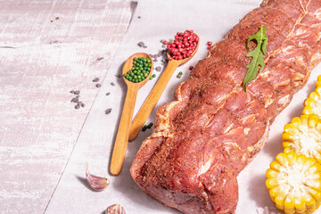 A piece of raw pork loin, marinated fresh meat tied with culinary twine, sweet corn and spices