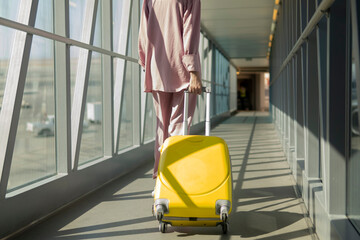 girl with a yellow suitcase walk through the terminal to the airport