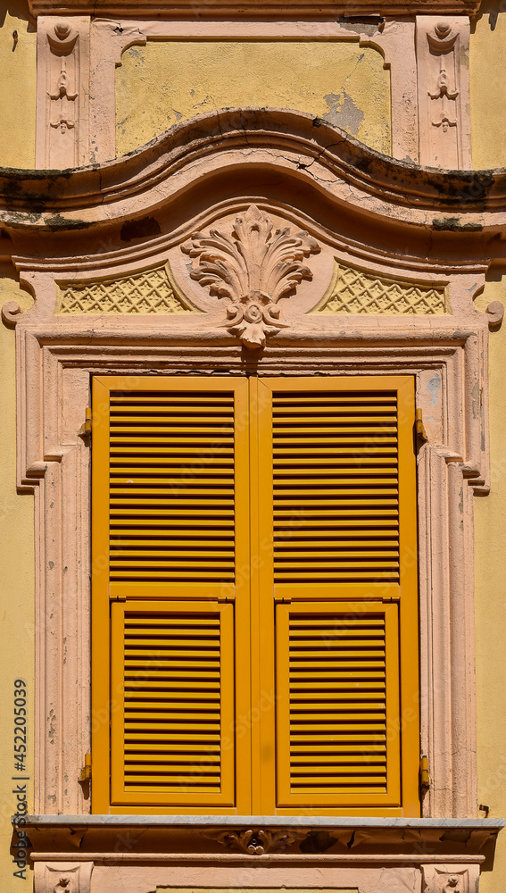 Wall mural Close-up of the closed window of an old palace with yellow shutters and bas-relief decoration, Italy