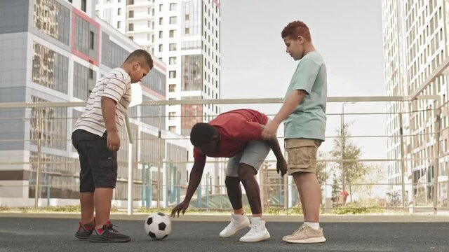 Full-length shot of African American man and his two teenage sons training football outdoors at sportsground, bouncing football with two feet