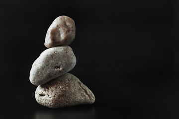 Three stones stand on top of each other keeping their balance. Dark background. Copy space..
