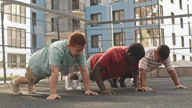 Athletic African American man and his two teenage sons doing push-ups together during outdoor training at sportsground