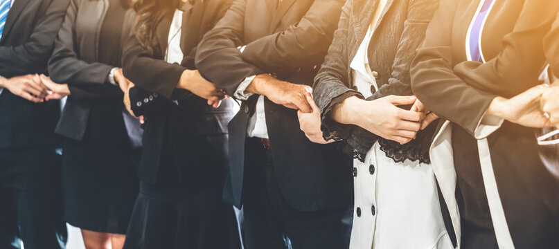 Many happy business people holding hands together with joy and success. Company employee celebrate after finishing successful work project. Corporate partnership and achievement concept.