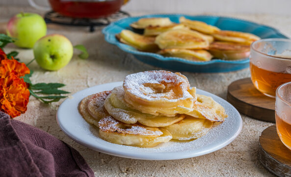 Dessert, fried rings of apples in batter on a white plate on a light concrete background. Apples recipes.