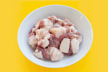 Cut streaky pork in white bowl on yellow background.