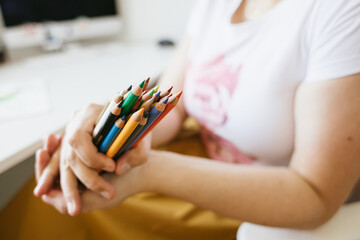 a bunch of colour pencils in woman's hands , computer desk in background - 452212874