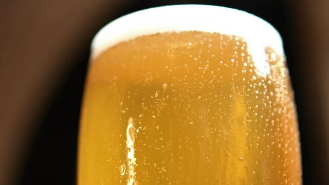  Beer sways in the glass, bubbles and foam rise. Cold Light Beer in a glass with water drops. Craft Beer forming waves close up.