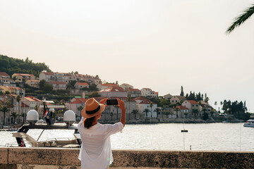 Girl tourist photographs the sea bay and buildings in Korcula town, Croatia - obrazy, fototapety, plakaty