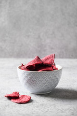 Vegetable beetroot chips in gray bowl on a gray background. Vegan snack. Close up. Vertical format.