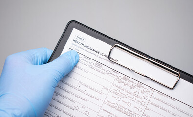 A hand in a medical glove points to a closeup text HEALTH INSURANCE written on a document.
