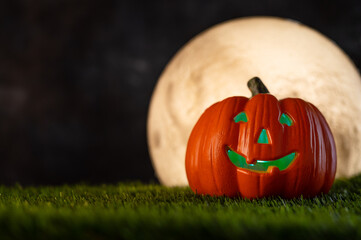 Halloween background. Smiling orange pumpkin on a green meadow, illuminated from the inside with green light. Night black sky and large white moon. Minimalism.Empty space to insert.