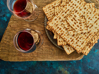 Two glasses of red wine and matzah - traditional Jewish bread. Simple brown mat and dark blue background. Feast of the Jewish Passover, Torah, religion, Judaism, rituals. kosher food.
