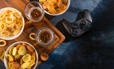 On a wooden stand, a traditional set of gamers - beer, chips, onion rings, a joystick. Concept -...