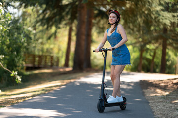 The transport of the future is an electric scooter. Happy smiling girl is riding in the park. Active rest, fun pastime, environmental protection, new technologies, popular transport.