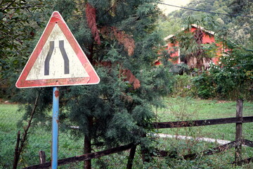 Verkehrszeichen Engstelle vor altem Holzzaun in idyllischer Landschaft im Sommer an einer...