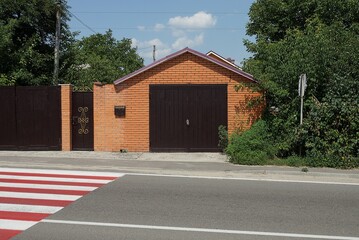 facade of a red brick garage with brown iron gates and part of a fence with a closed door on a street by a gray asphalt road
