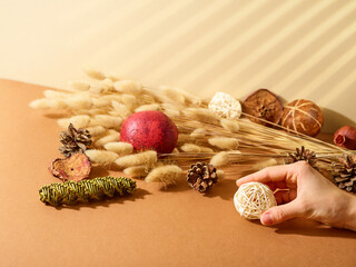 Composition for interior decoration. Cereals, toys, cones. A female hand holds a Christmas tree toy. Handmade. New Year and Christmas decor, decor for family holidays.