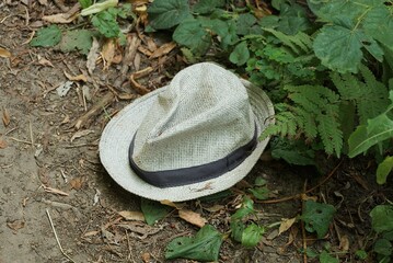 one white summer cloth hat lies on gray ground among green leaves of plants outside