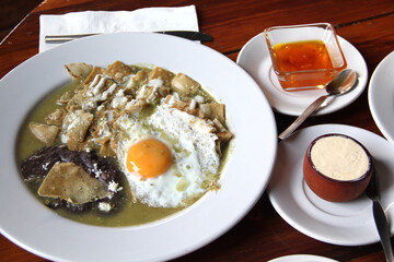 Delicious Mexican breakfast with coffee, sweet bread, beans, chilaquiles, butter, jam, sugar, fried egg, omelette
