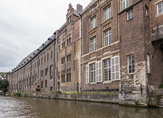 Fototapeta na wymiar Gent, Flanders, Belgium - July 30, 2021: Brown brick back facade along Leie River of former medieval Dominican Cloister, now University center. Famous during Protestant revolution in 16th century.