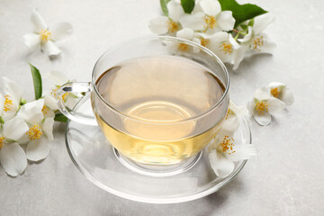Glass cup of jasmine tea and fresh flowers on grey table