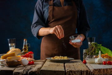 The chef prepares a classic Caesar salad. He salt the chicken fillet in a bowl. Lots of ingredients. Healthy lifestyle, festive dish. Restaurant, hotel, cafe, home cooking, recipe book.