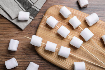 Sticks with delicious puffy marshmallows on wooden table, flat lay