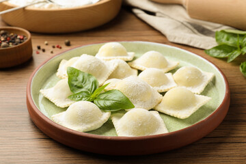 Uncooked ravioli and basil on wooden table