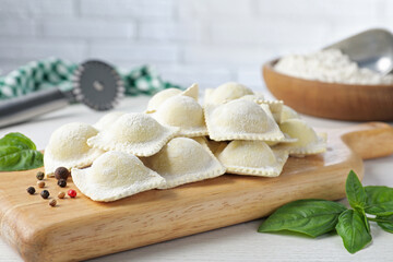 Uncooked ravioli, peppercorns and basil on white wooden table, closeup