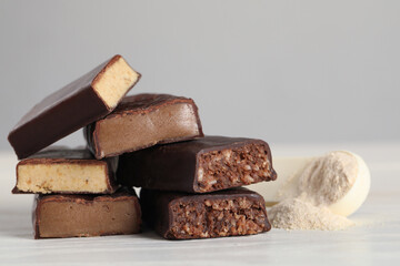 Pieces of tasty bars and spoon with protein powder on white table