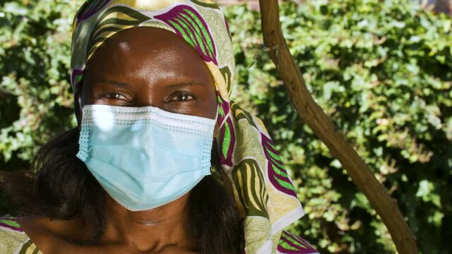 African woman outside wearing traditional clothes and a face mask during COVID-19 Coronavirus pandemic in Africa