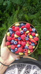 Plate with delicious berries in hand. Red raspberries, blueberries, white and red strawberries.