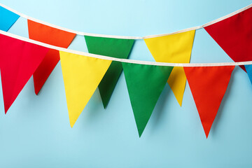 Fototapeta na wymiar Buntings with colorful triangular flags hanging on light blue background. Festive decor