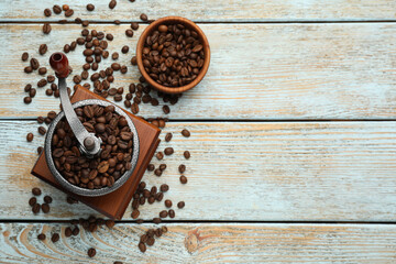 Vintage manual coffee grinder with beans on light wooden table, flat lay. Space for text