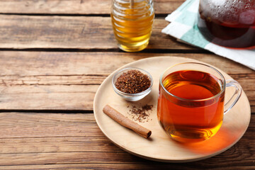 Freshly brewed rooibos tea, dry leaves and cinnamon stick on wooden table. Space for text