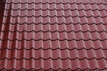 The roof of a private house with metal tiles of burgundy color.