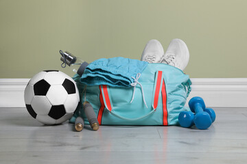 Bag with different sports equipment on wooden floor indoors
