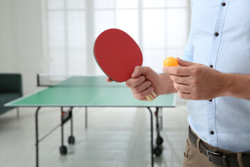 Businessman with tennis racket and ball near ping pong table in office, closeup. Space for text