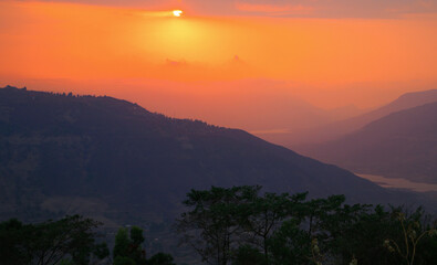 A sunset with deep orange saffron  sky over the mountains crossing each other and valley overlooking the trees