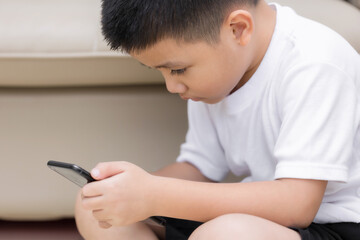 Fototapeta premium Little boy having fun playing game on mobile phone, Preschool kid sitting on sofa with smiling face watching cartoon on smartphone, Child using cell phone while relaxing at home