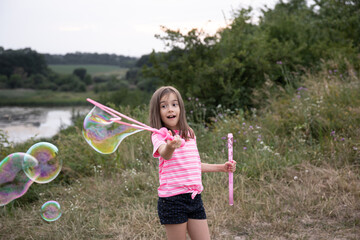 A little girl blows large, colorful soap bubbles in the nature.