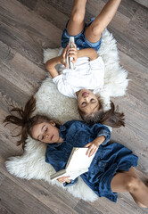 Little girls sisters read books lying on the floor, top view.