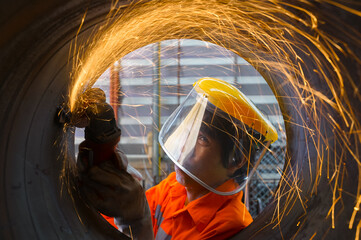 Highly skilled workers wearing industrial uniforms and Welded Iron Mask at Steel use electric wheel grinding on steel structure in the construction industrial factory.industrial safety first concept